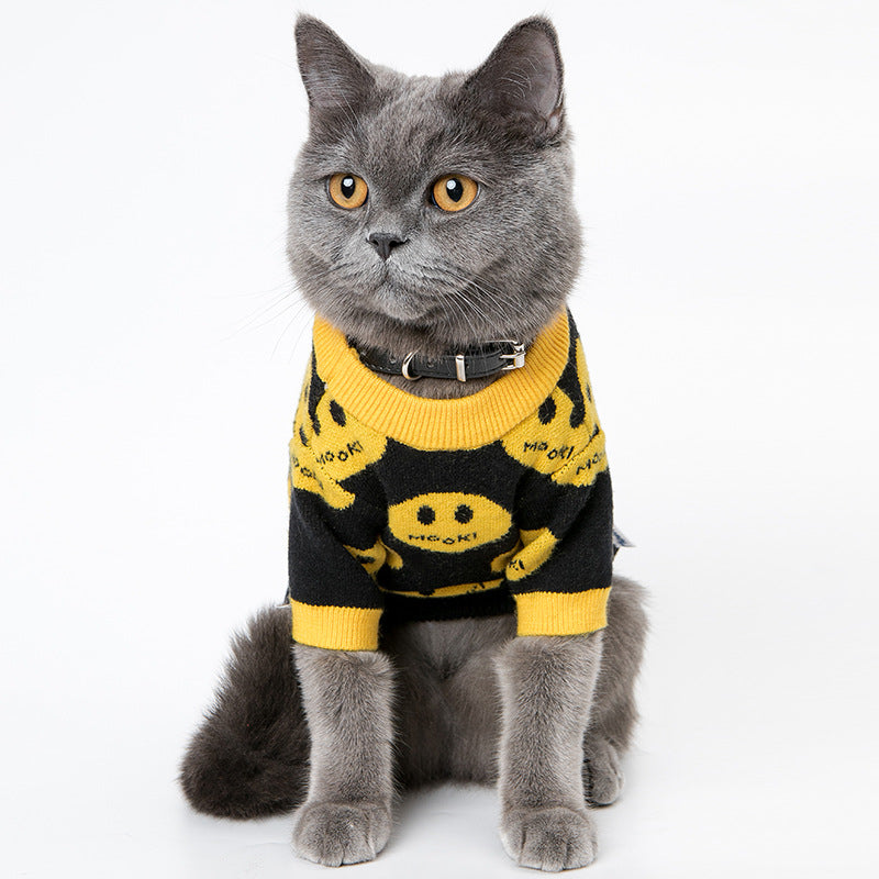 Cat wearing a black and yellow sweater with smiley face patterns on a white background